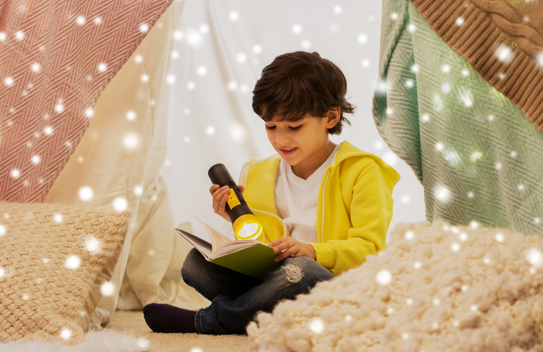 A child reading a book by flashlight in a cosy blanket fort